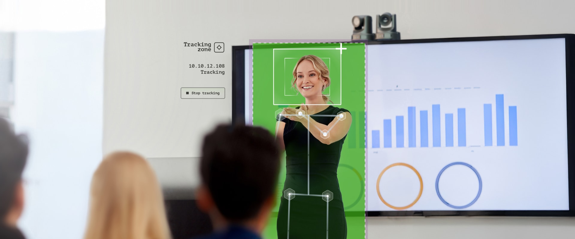 A presenter delivers a presentation to an audience in a modern conference room. The presenter is highlighted with a green overlay, indicating Q-SYS VisionSuite Intelligent Presenter Tracking technology. Behind them, a large screen displays a bar chart and circular graphics. Text on the screen reads “Tracking zone” with tracking status information. This image demonstrates the use of Q-SYS’ VisionSuite Intelligent Presenter Tracking technology to enhance presentation engagement and interactivity.