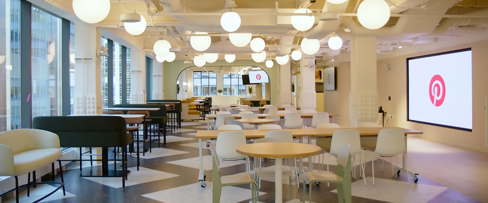 Modern open-plan office with Pinterest branding, featuring communal tables and spherical lighting.