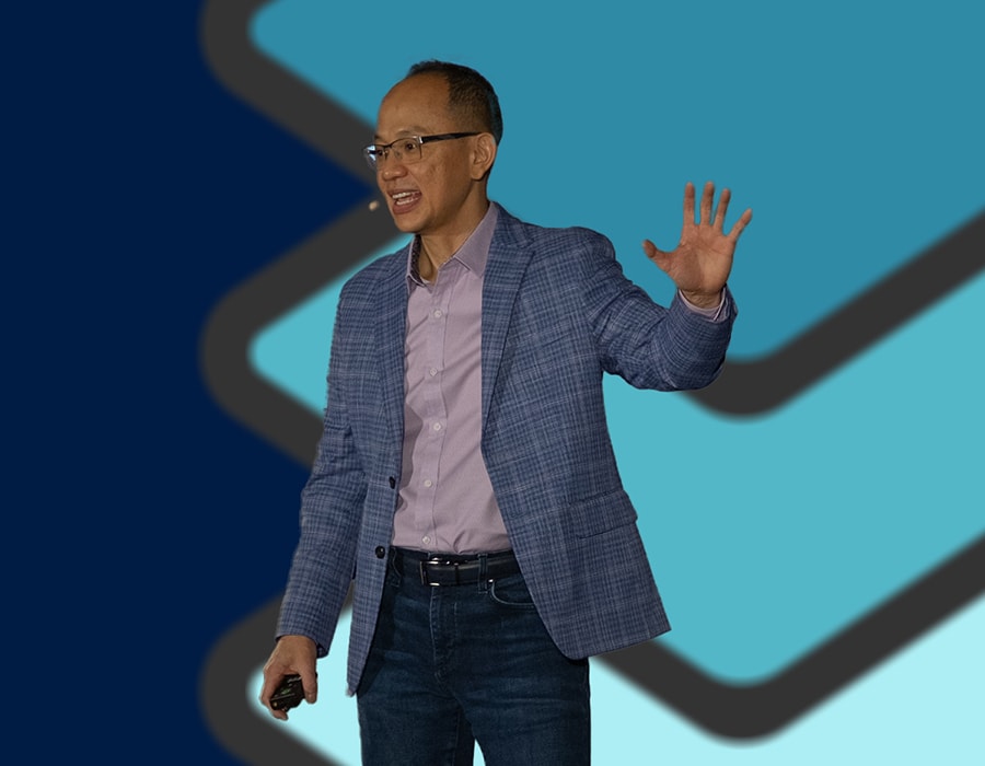 QSC Chairman of the Board and CEO Joe Pham in blue jacket gesturing while speaking against a blue background.